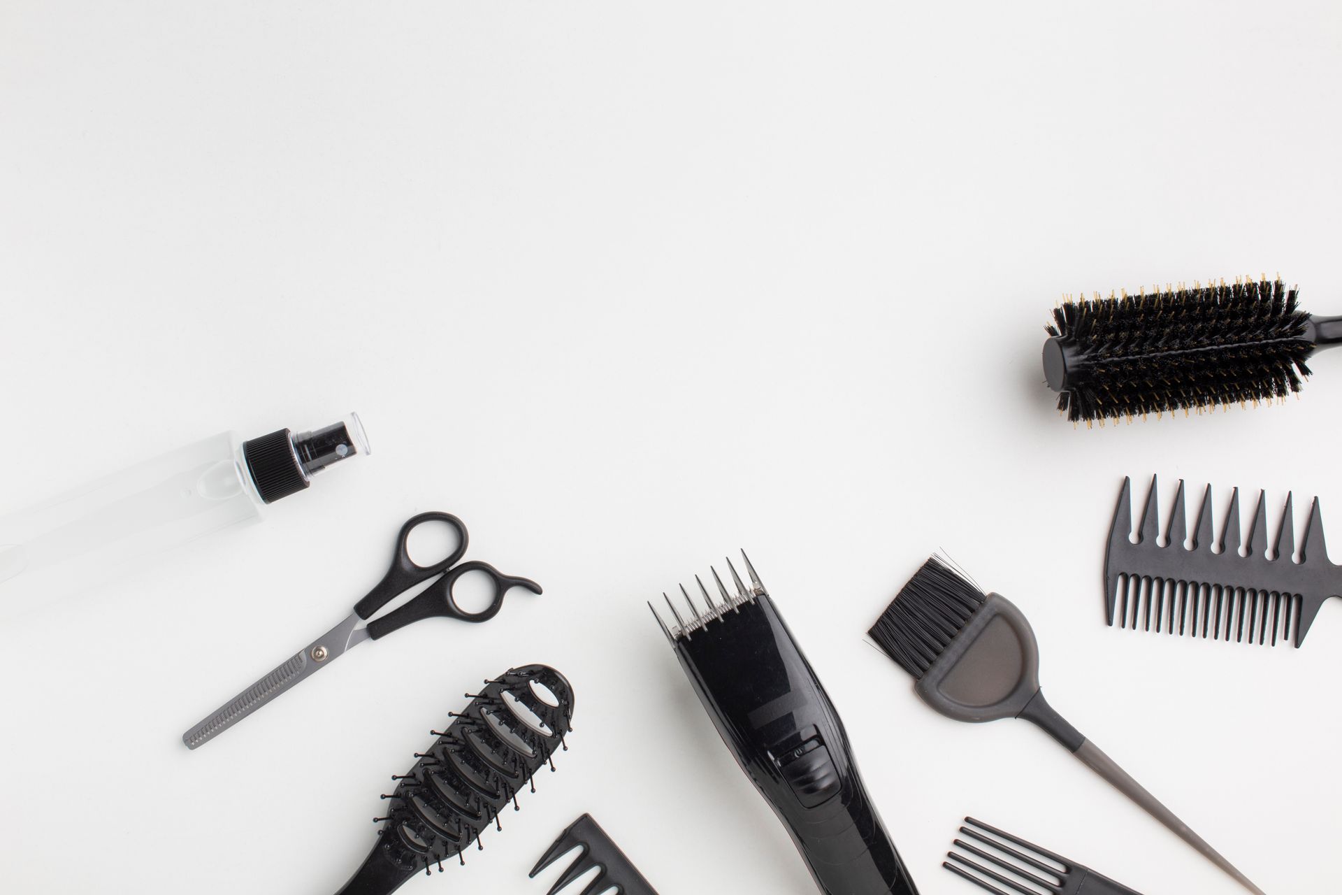 Herramientas para peinar el cabello de color negro dispuestas sobre un fondo blanco; incluye tijeras, peines, cepillos y una botella de spray.