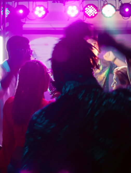 People dancing under pink and white stage lights at a club.