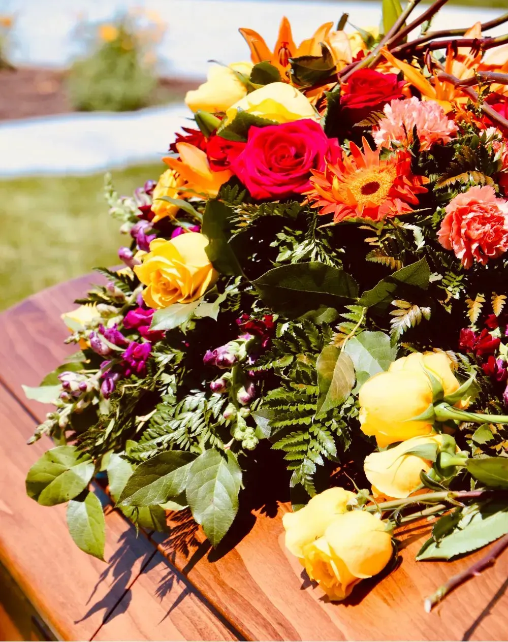 Colorful flower arrangement on a wooden surface, outdoors, with yellow, red, and orange blooms.