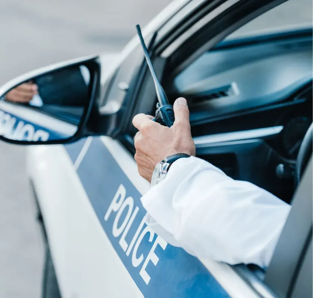 Police officer in car holding a walkie-talkie, side view. Blue and white police car visible.