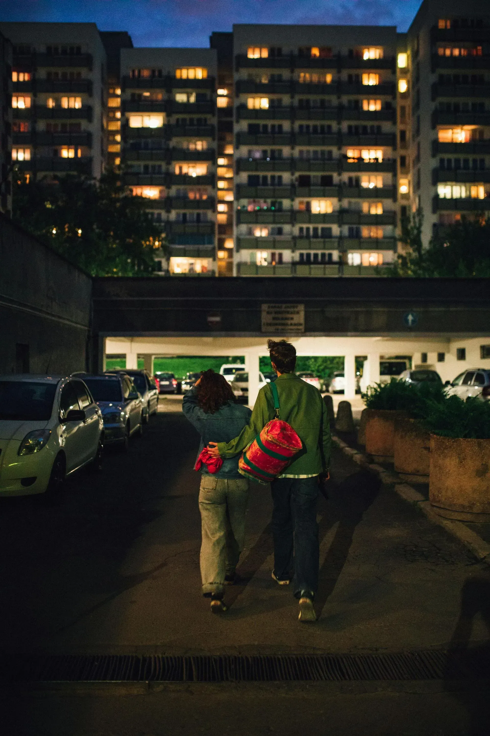 Couple walking arm-in-arm at night with glowing apartment building in the background.