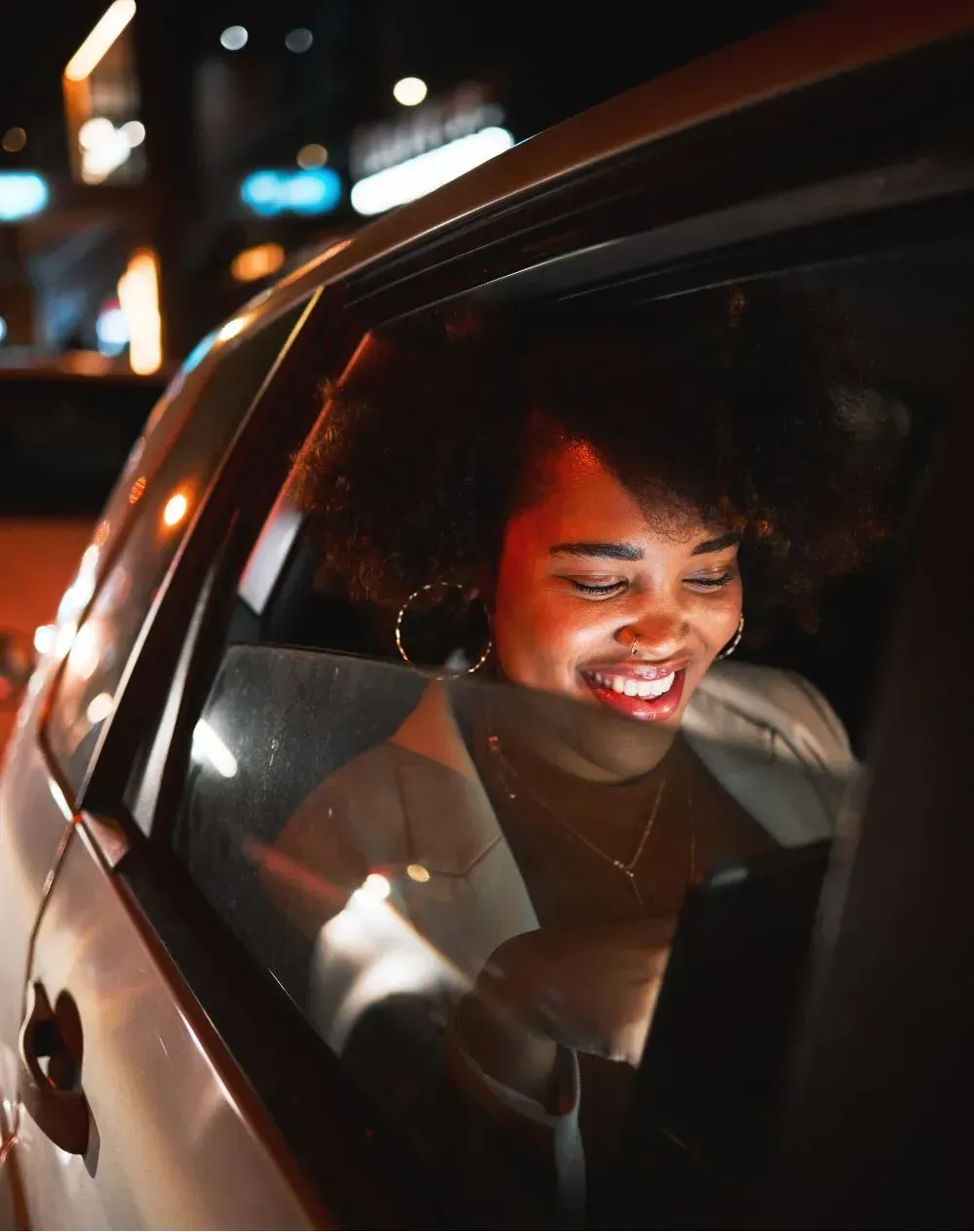Woman in car smiling at phone, night setting.