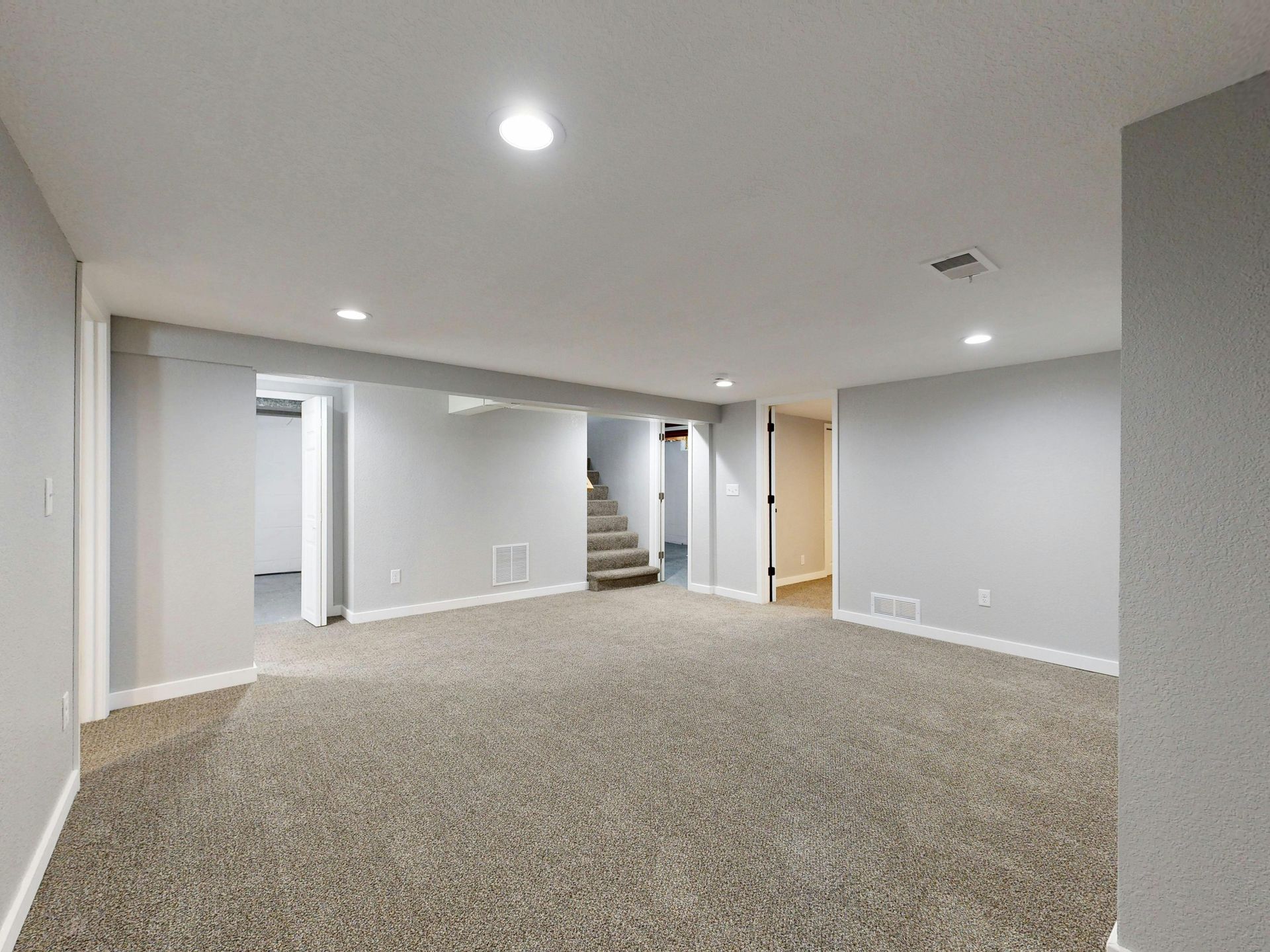 Empty basement room with gray walls, carpet, and recessed lighting.