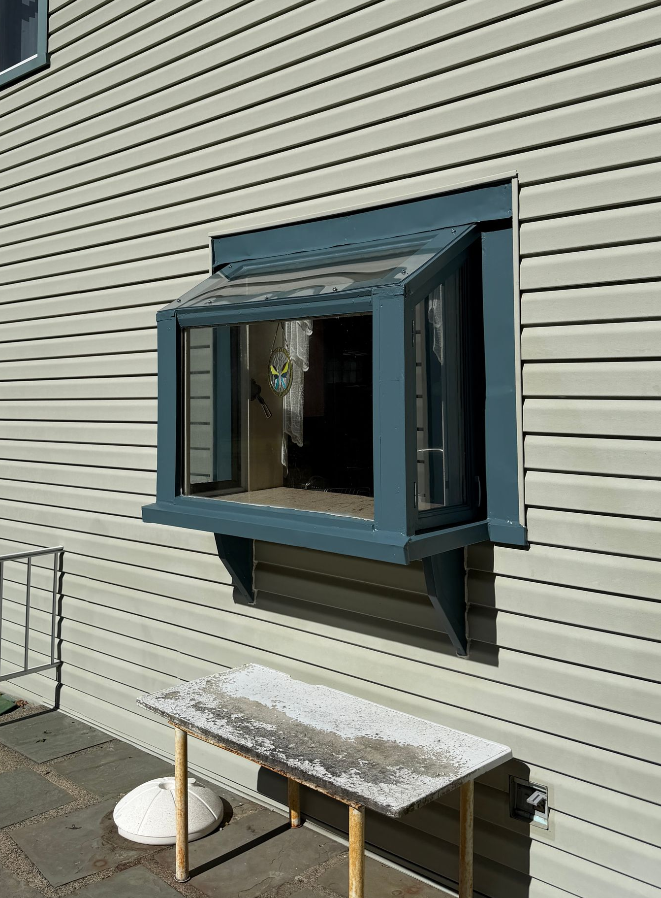 Long rectangular table, painted light gray, on a black metal base, in a garage. Paint supplies visible.