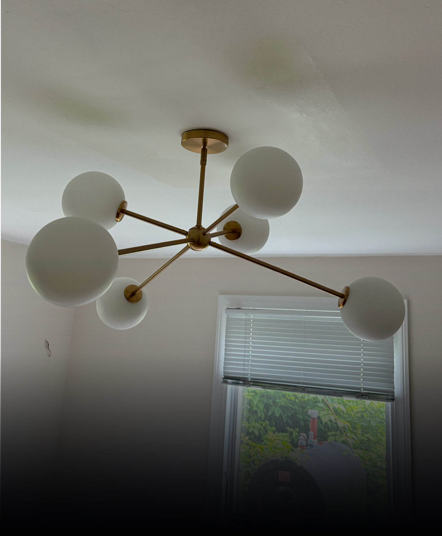 A brass-finished, mid-century modern style ceiling light fixture with six globe-shaped white glass bulbs.