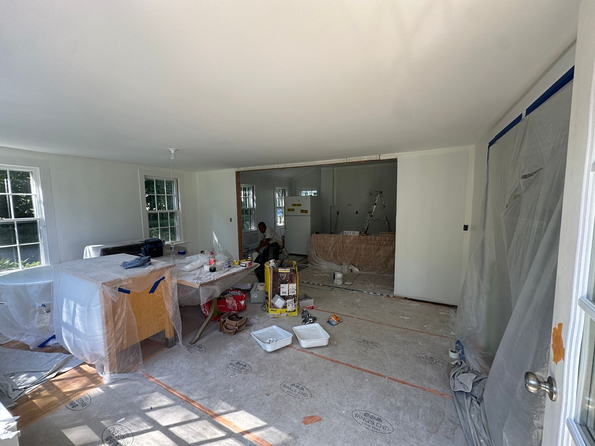 Long rectangular table, painted light gray, on a black metal base, in a garage. Paint supplies visible.