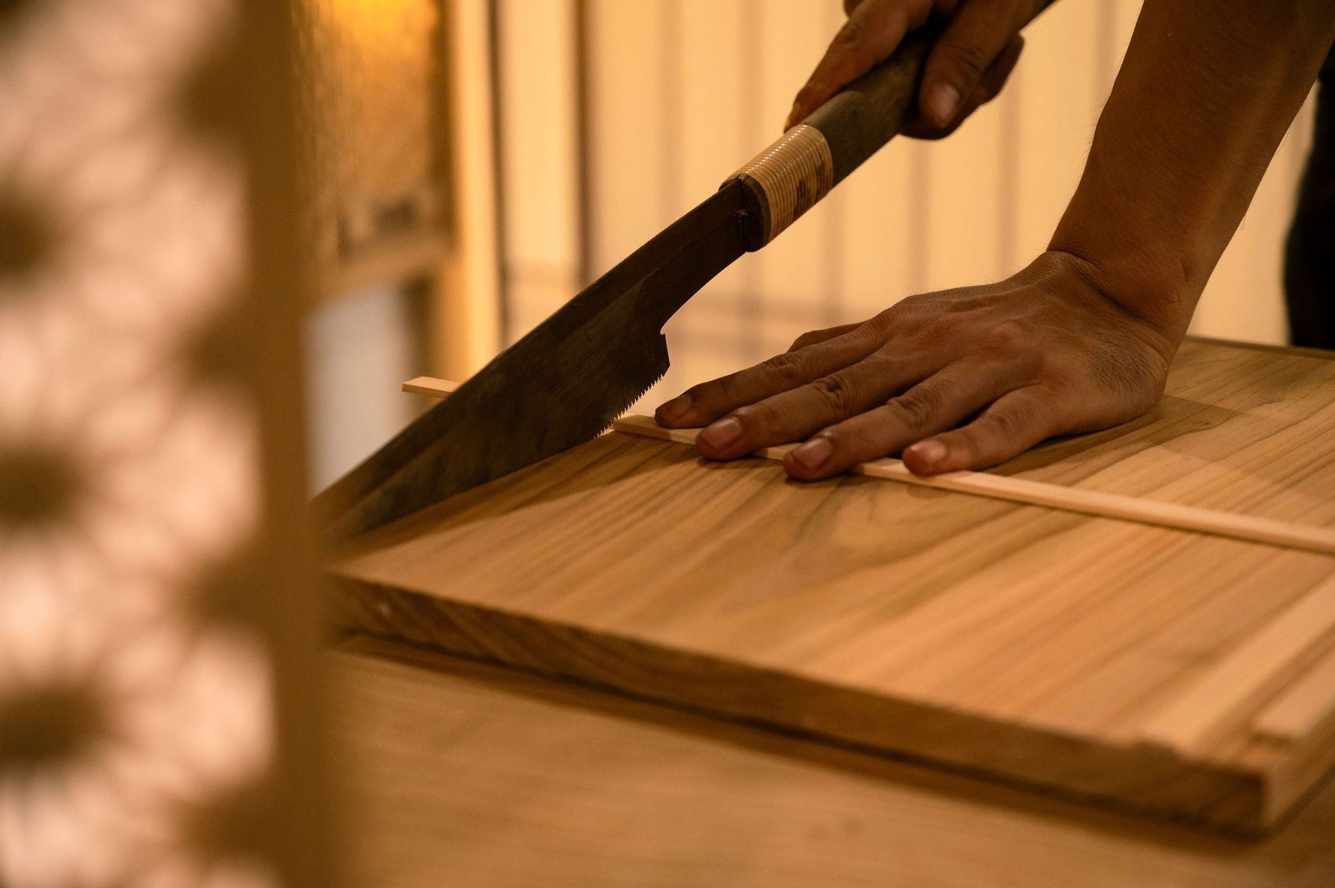 Hands cutting a wooden cutting board with a saw on a workbench