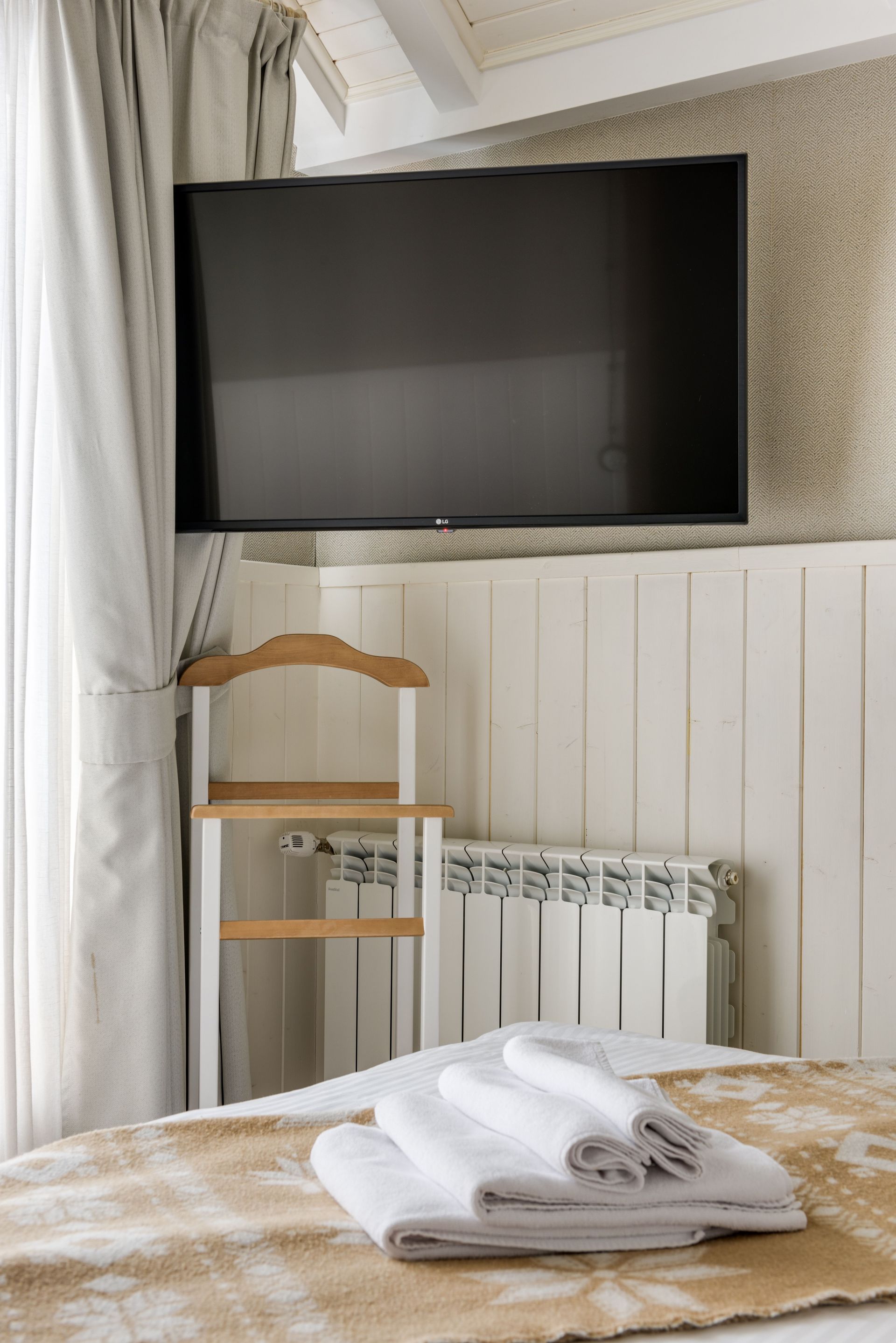 Bedroom with wall-mounted TV, radiator, wooden chair, and bed with folded towels.