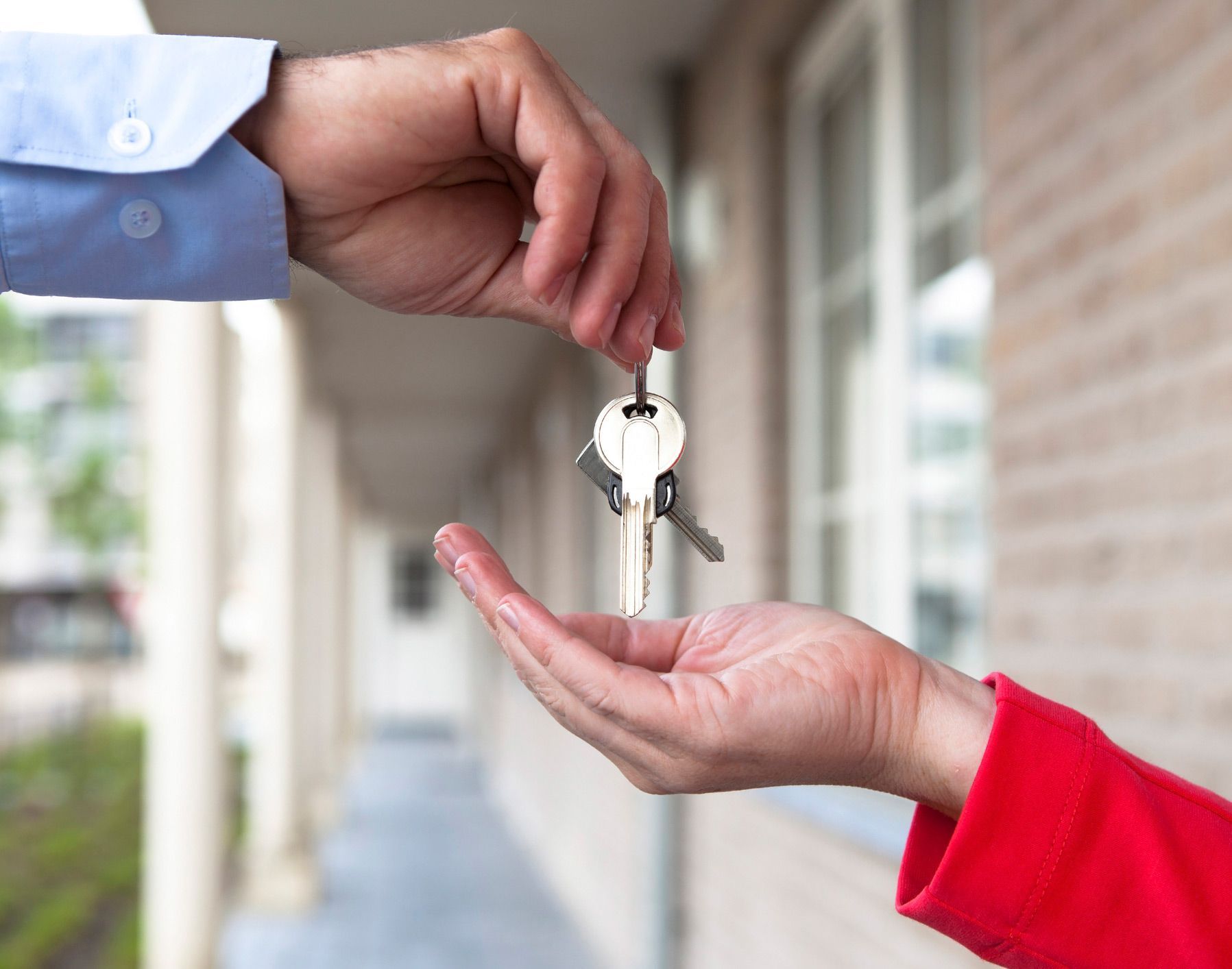 A man is handing a key to a woman in front of a house.