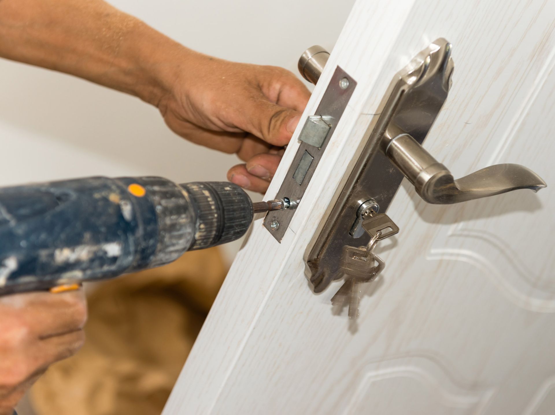 A man is using a drill to fix a door lock.