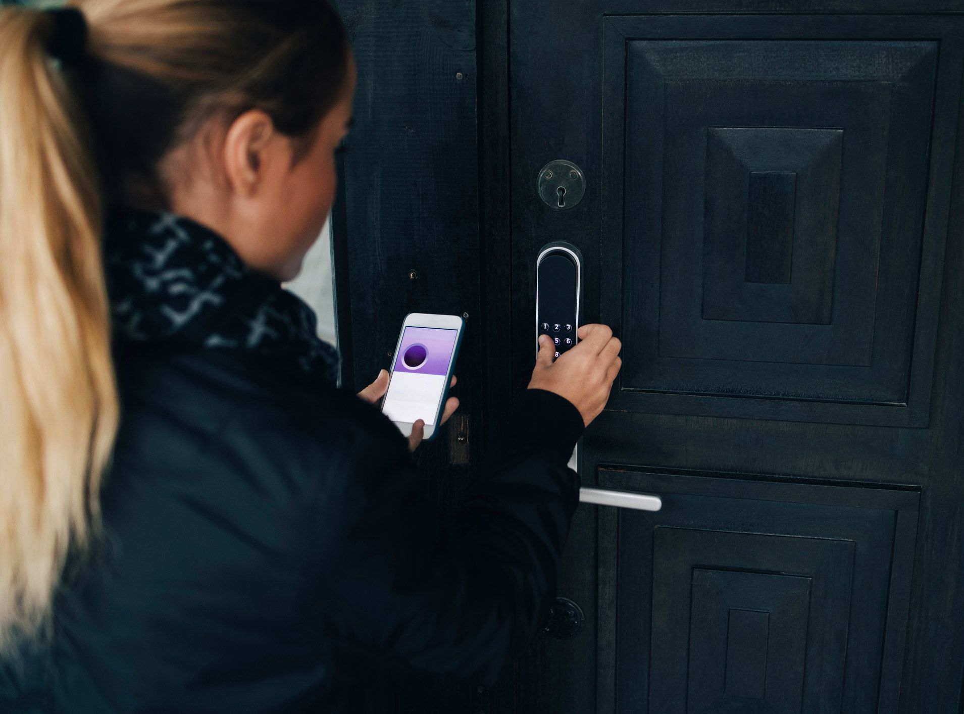 A woman is using a smart phone to lock a door.