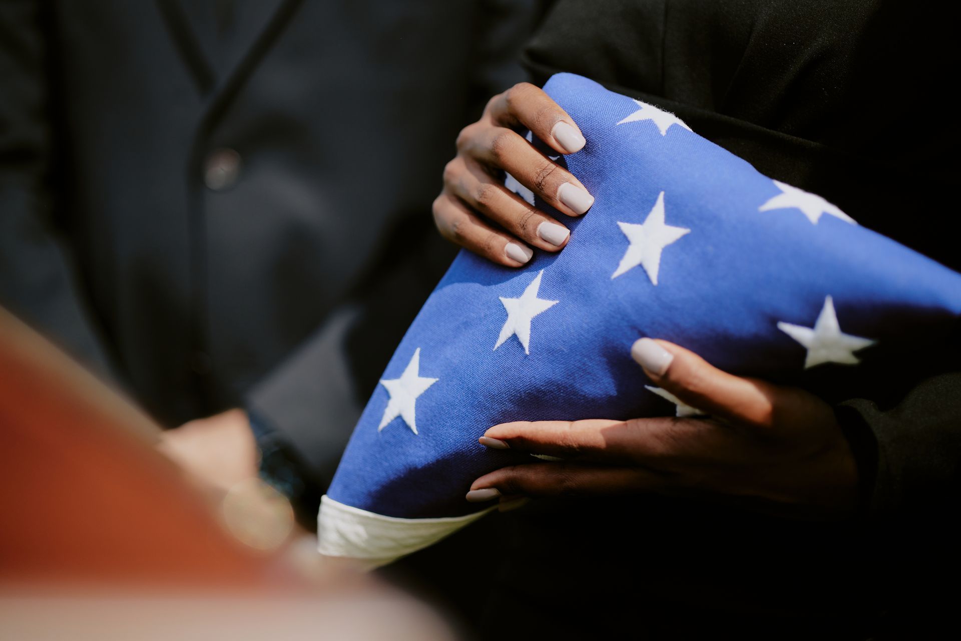 Hands hold a folded American flag during what appears to be a solemn, formal ceremony.