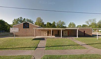 A brick church building with a flat, covered entrance and a sign in the front yard against a blue sky.