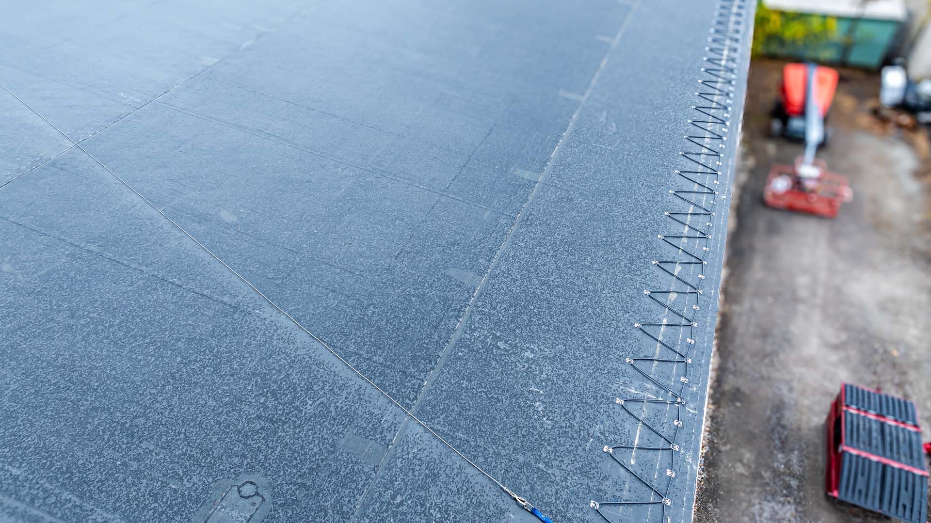 Close-up of a black flat roof with a zig-zag pattern of silver fasteners along the edge