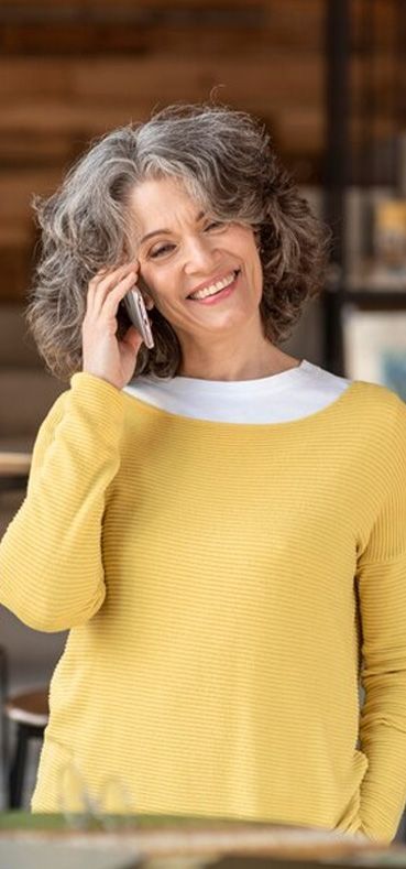 a woman in a yellow sweater is talking on a cell phone is happier after being treated for depression at Wasatch TMS in Heber City Utah