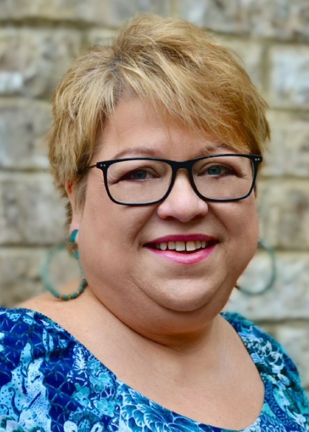 A woman wearing glasses and earrings is smiling for the camera.