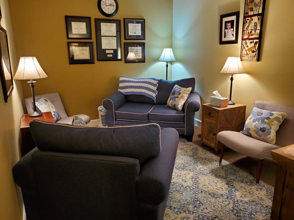 A living room with a couch , chair , lamps and a clock on the wall.