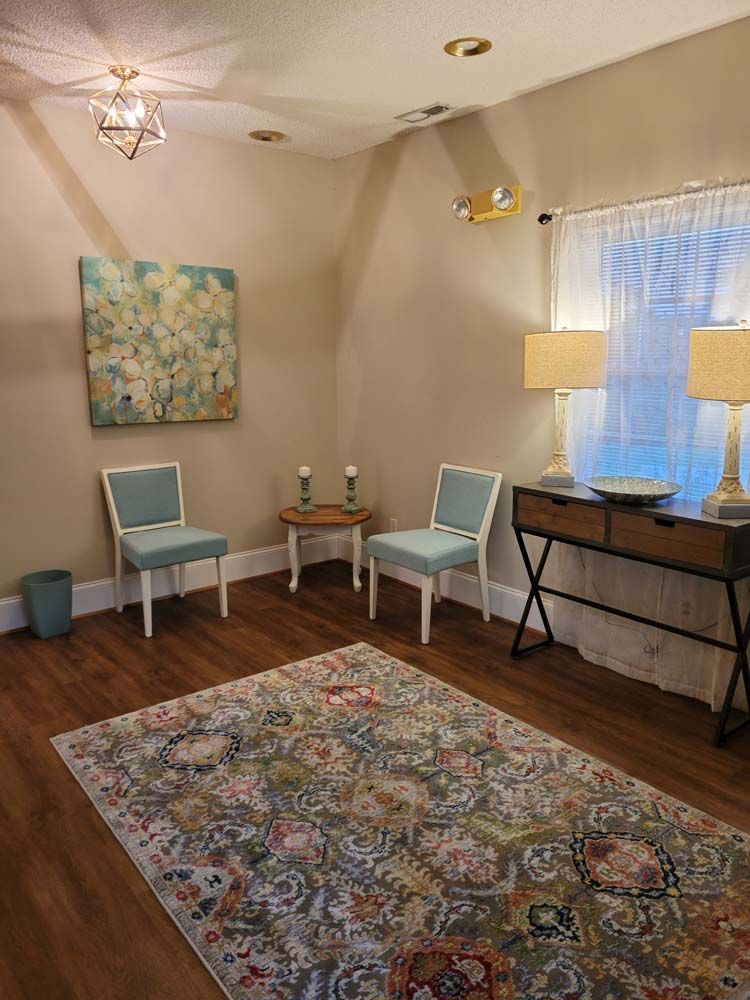 A room with two chairs , a rug , a table and a window.