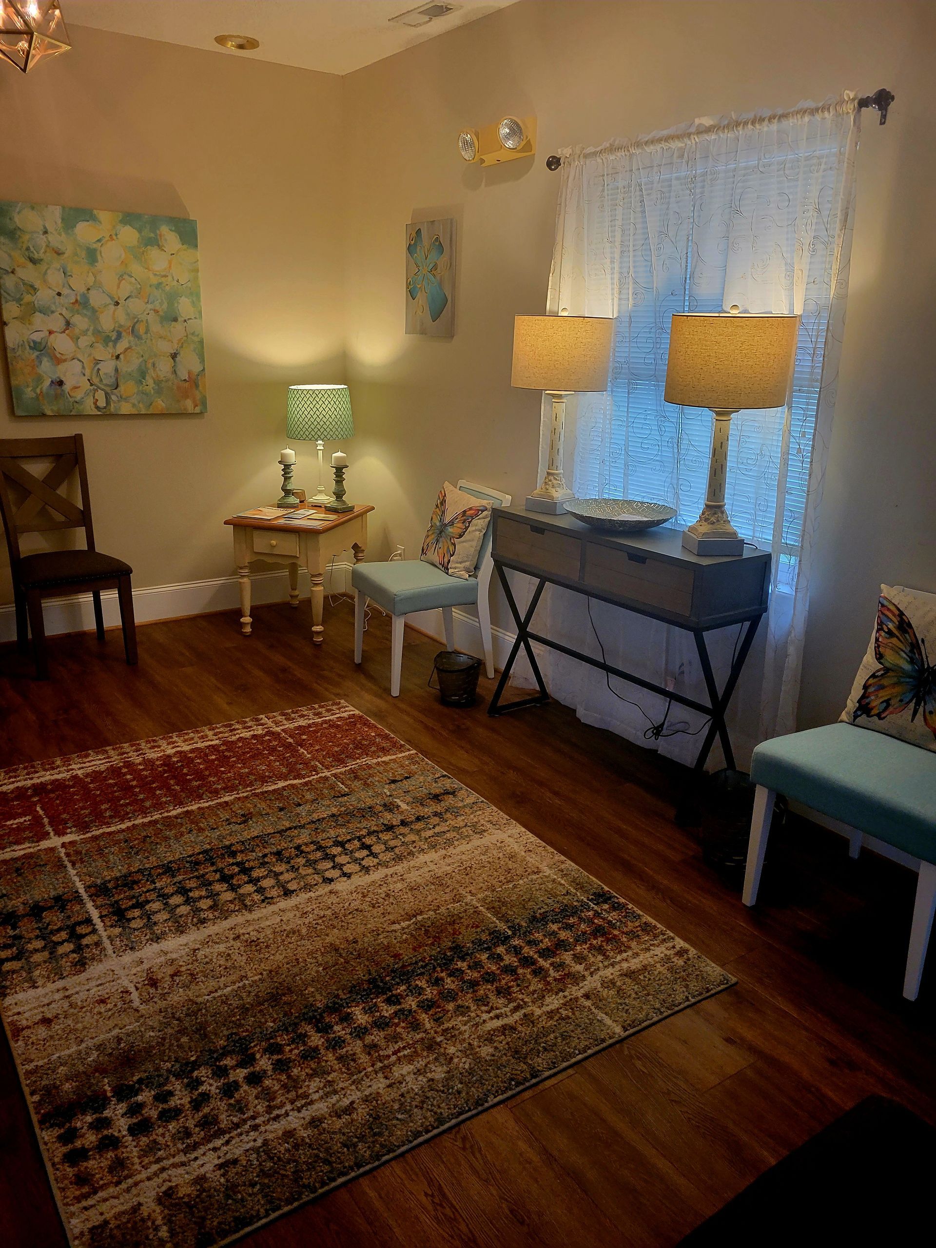 A living room with a rug , chairs , lamps and a window.