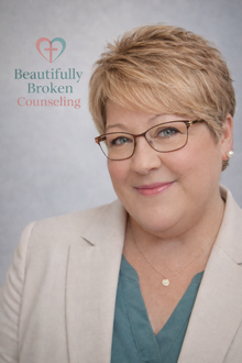 A woman wearing glasses and earrings is smiling for the camera.