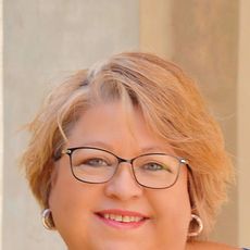 A woman wearing glasses and earrings is smiling for the camera.