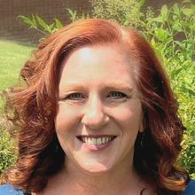 A woman with red hair is smiling and wearing a blue shirt