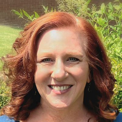 A woman with red hair is smiling and wearing a blue shirt