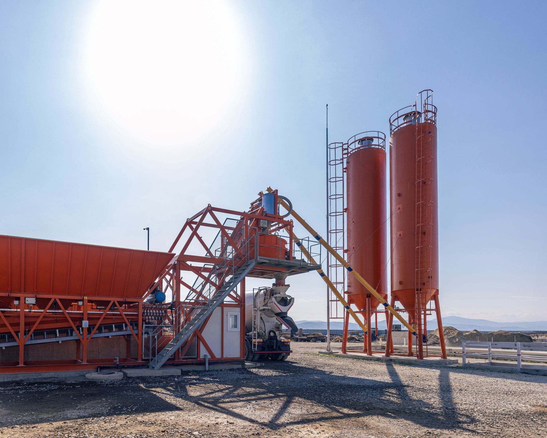 Orange concrete mixing plant against a bright sky.