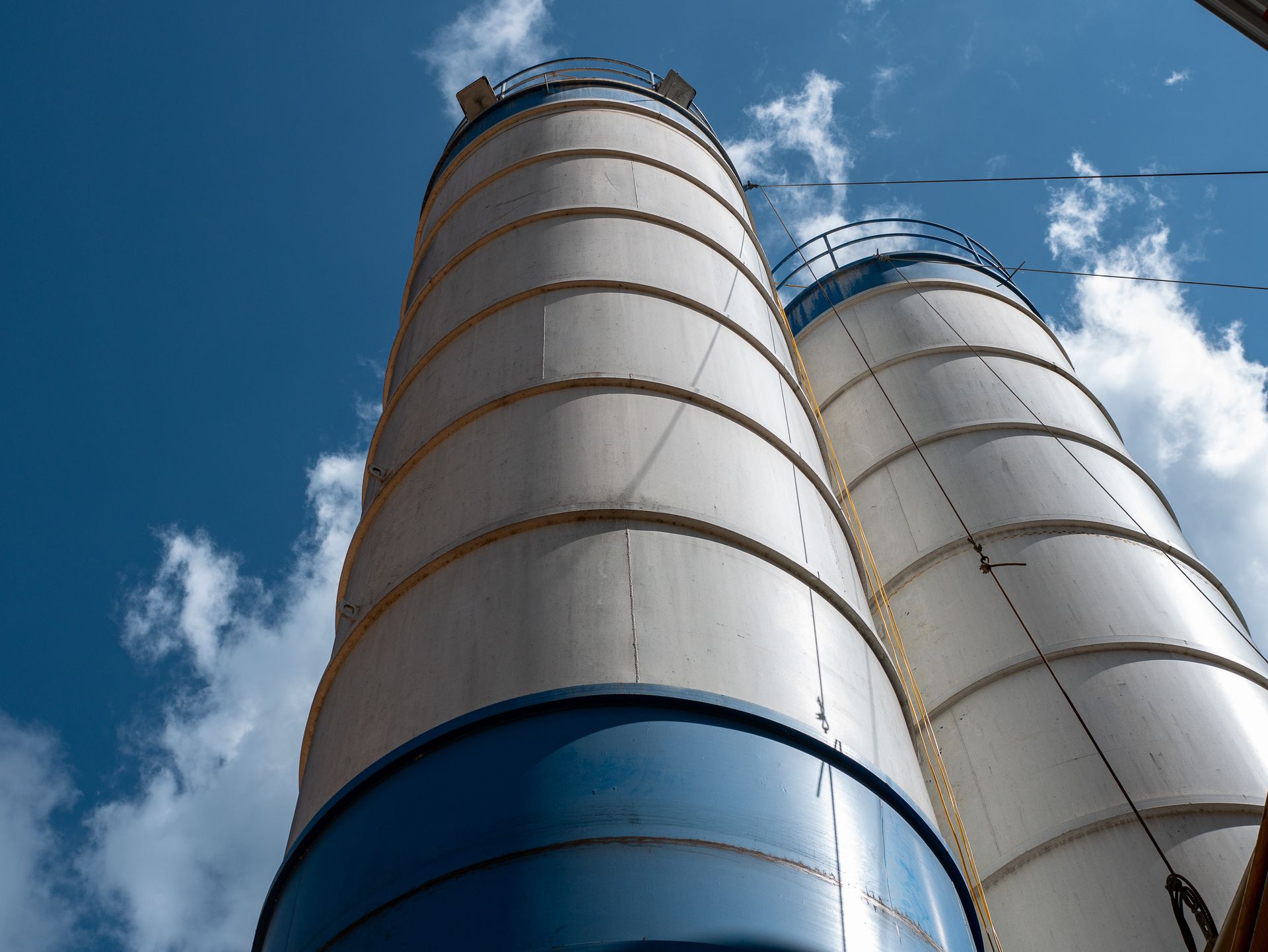 Two tall, white industrial silos with blue accents against a blue sky with clouds