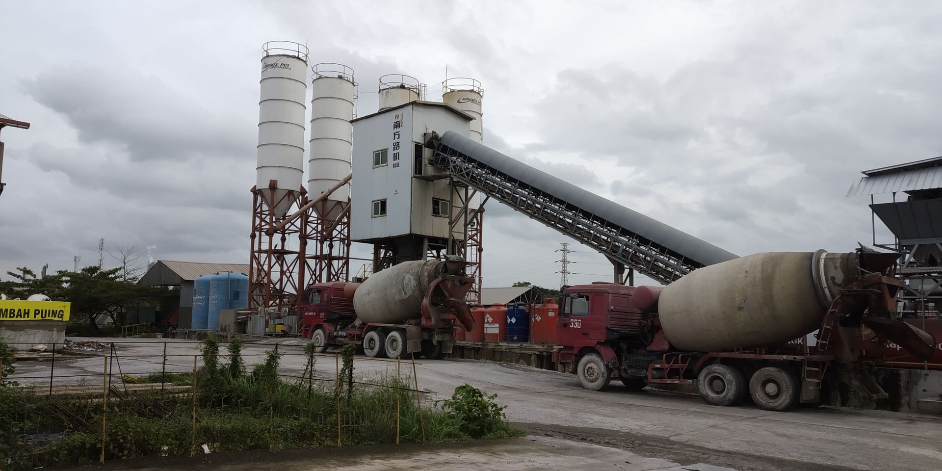 Concrete plant with two mixer trucks loading under a cloudy sky.