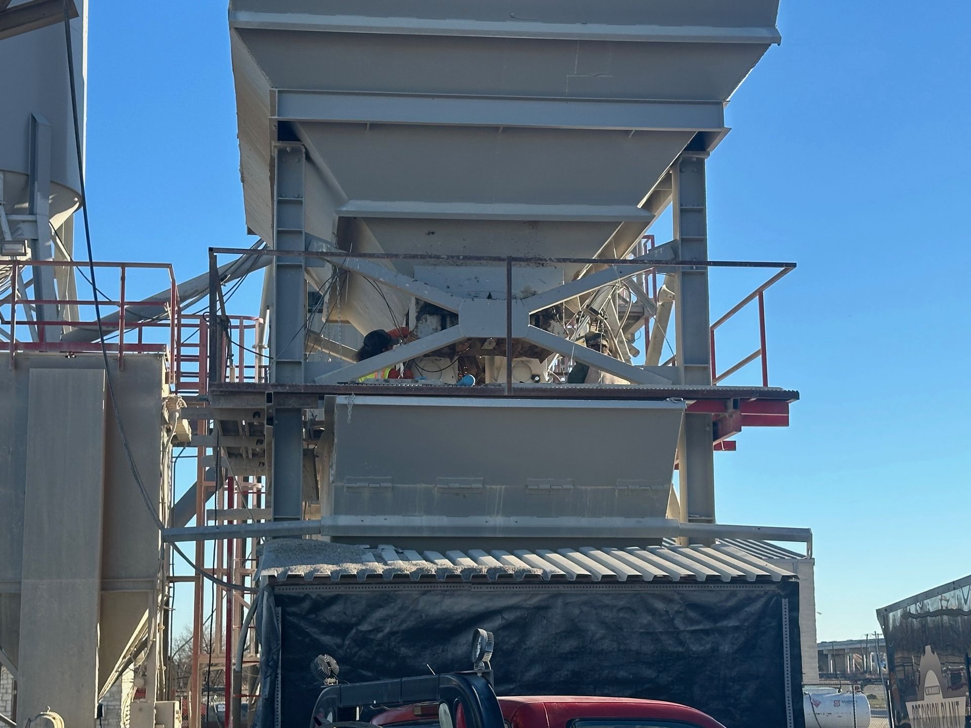 Industrial plant with scaffolding, bins, and a red vehicle below against a blue sky