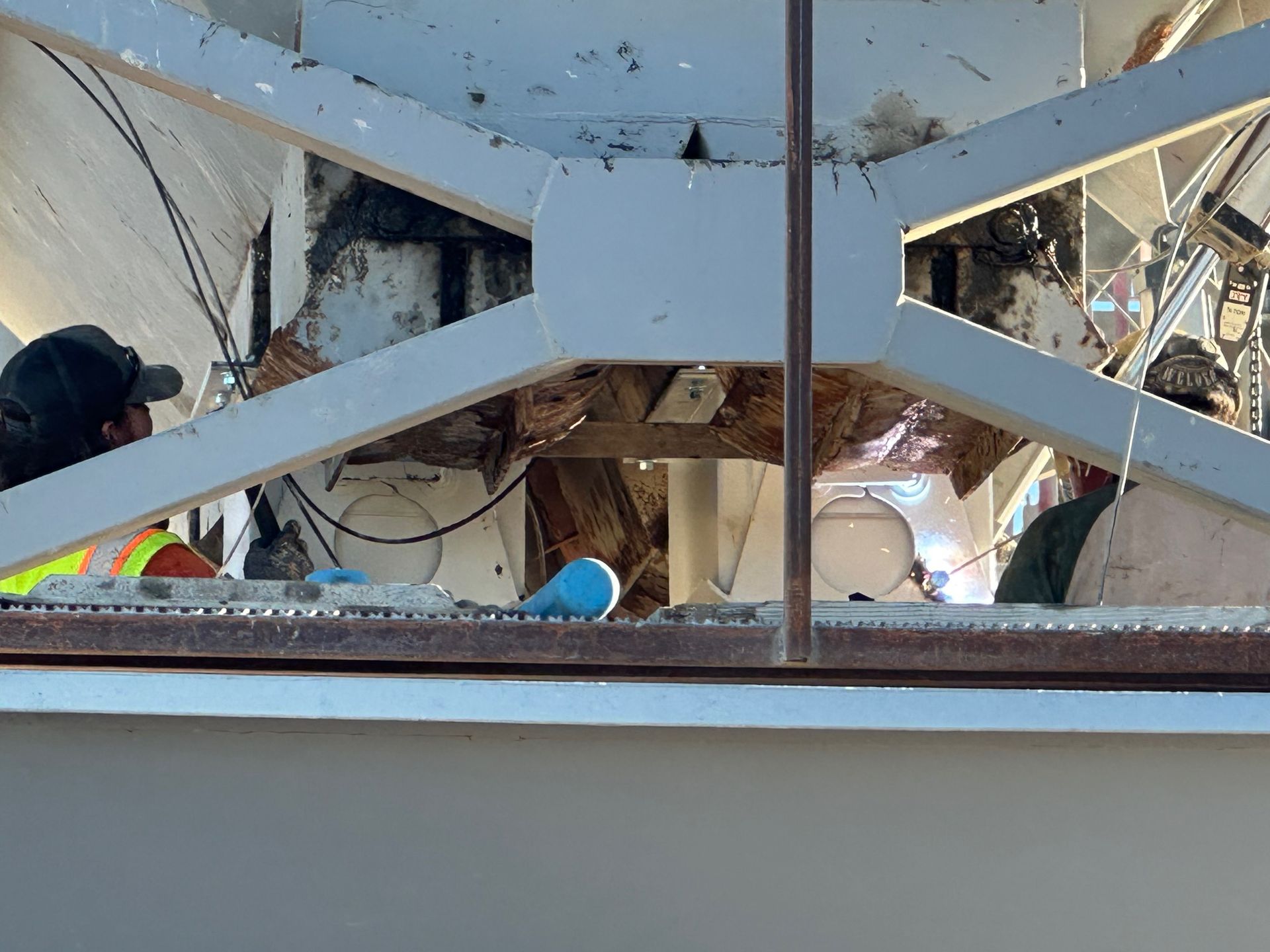Workers inspecting a white metal structure with support beams. One worker wears a hard hat