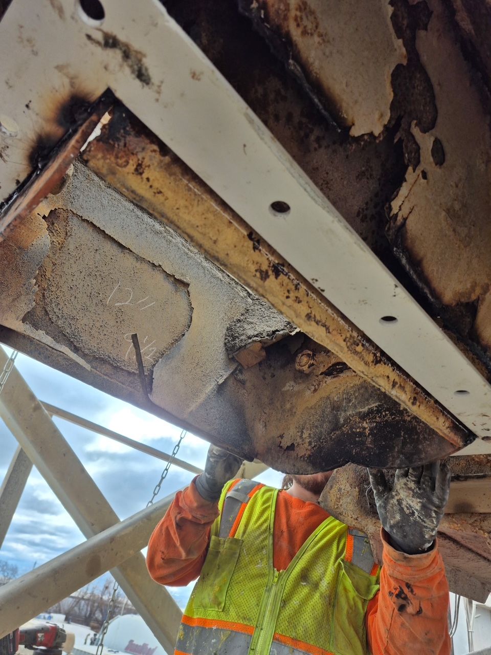 Person in safety vest inspects rusty, metal machinery from below