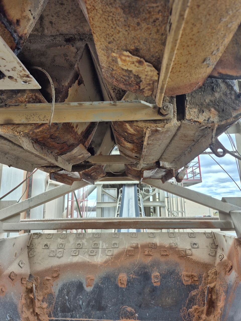Rusting industrial equipment, viewed from below, with metal beams and structures