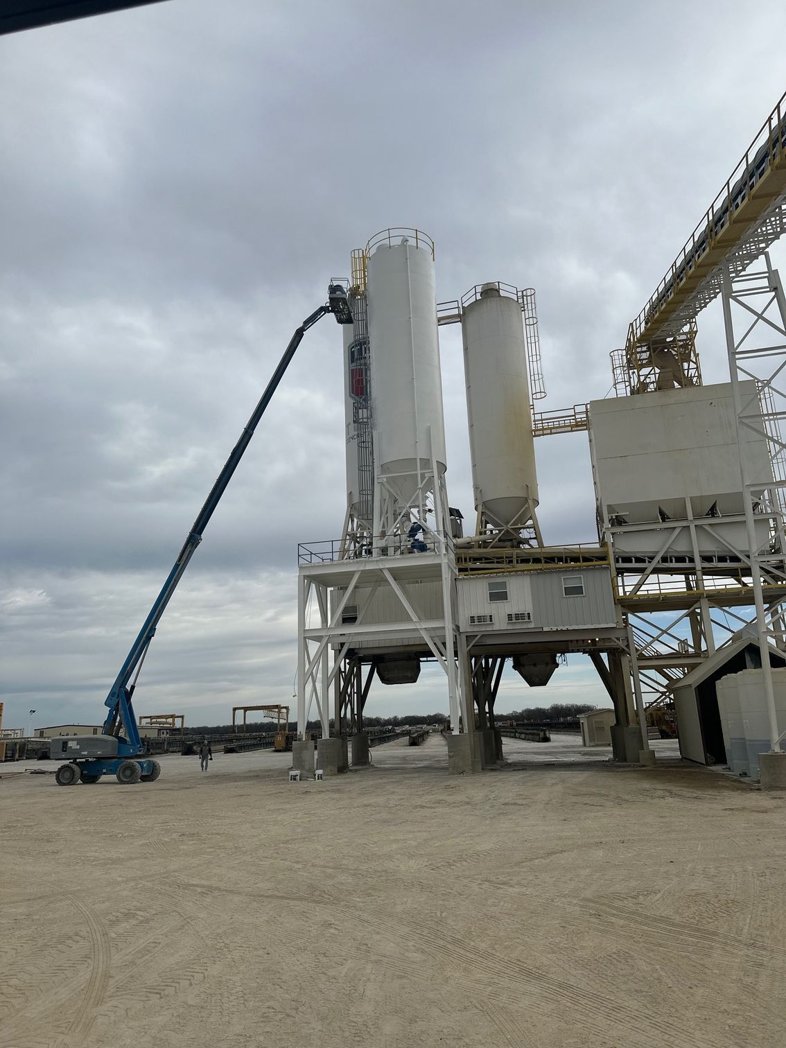 Blue construction lift extends toward white industrial silos