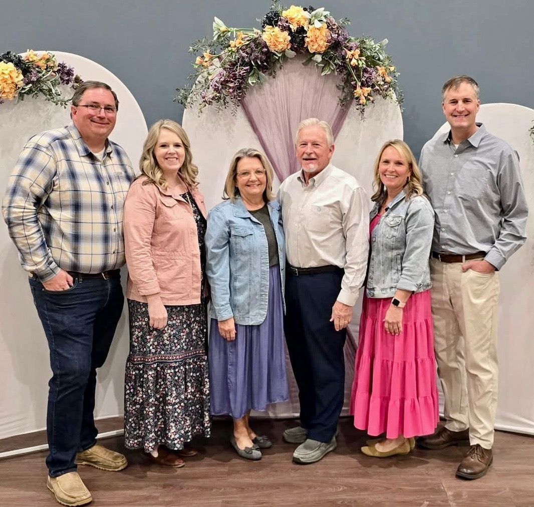 A group of people are posing for a picture in front of a floral arch.