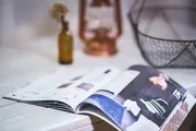 Open magazine on white table, with blurred decorative objects in background.