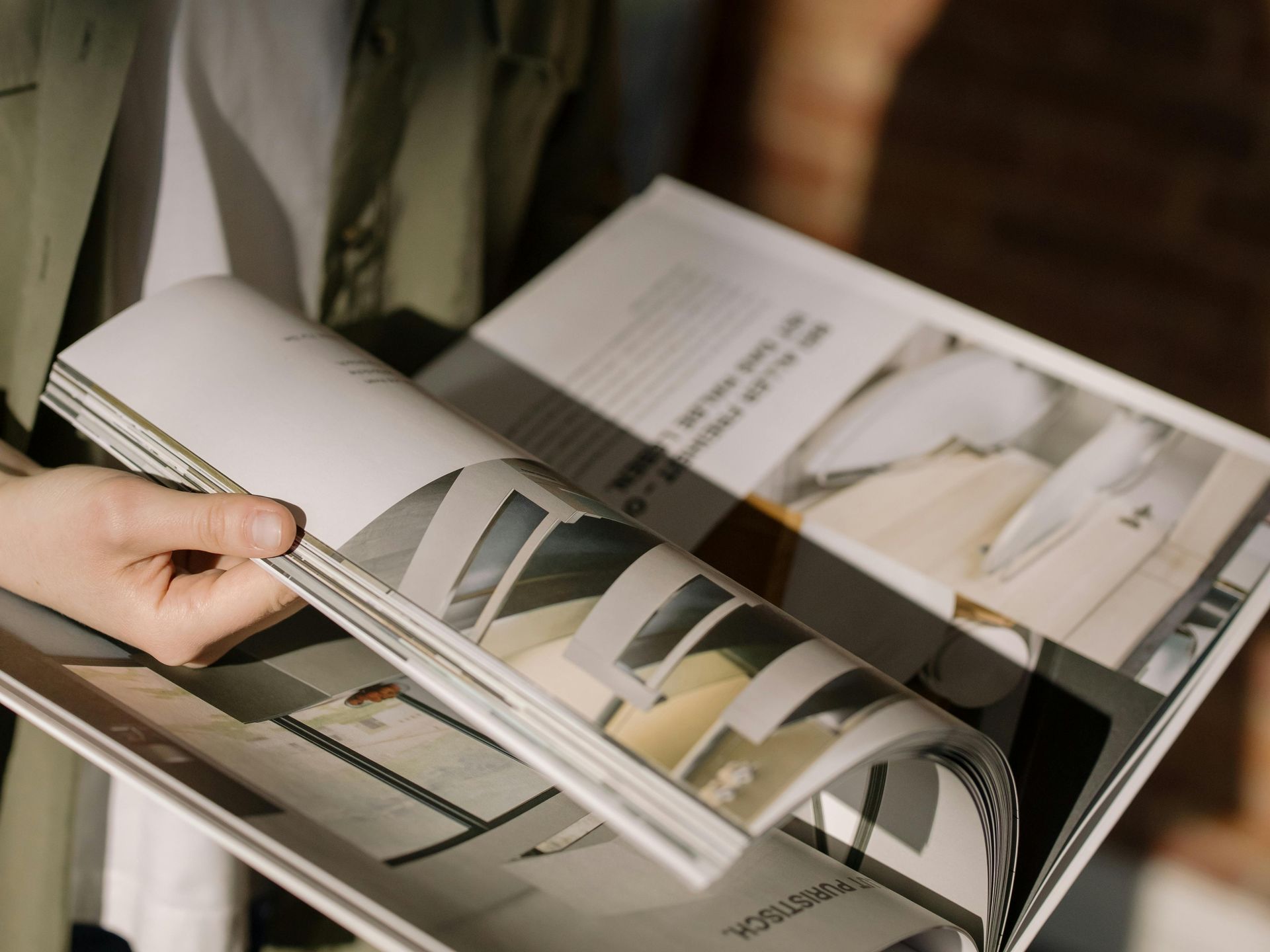 Person holding open magazine, flipping pages, interior design photos visible.