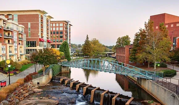 Brick clock tower in a snowy downtown square under a blue sky, with buildings and bare trees nearby