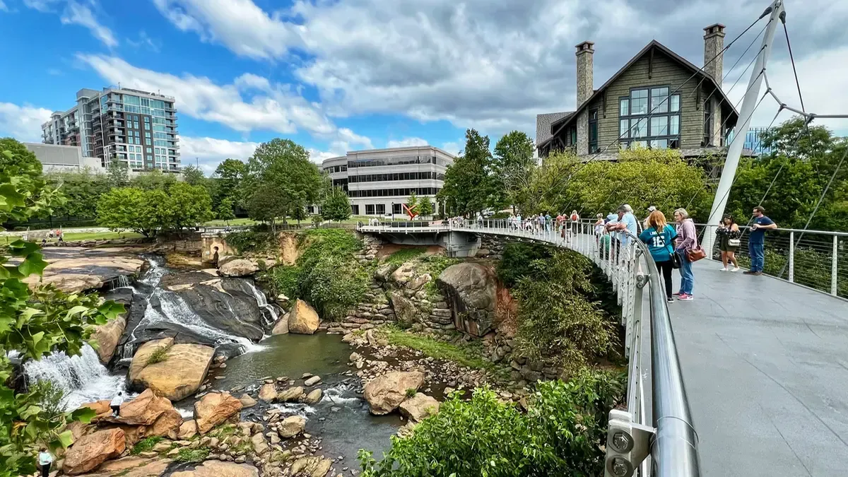 Brick clock tower in a snowy downtown square under a blue sky, with buildings and bare trees nearby