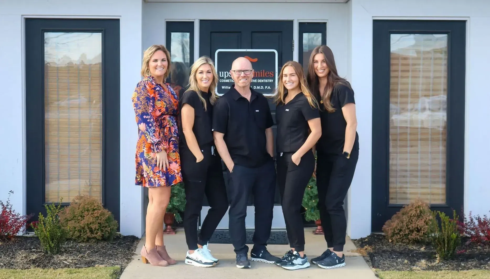 Brick clock tower in a snowy downtown square under a blue sky, with buildings and bare trees nearby