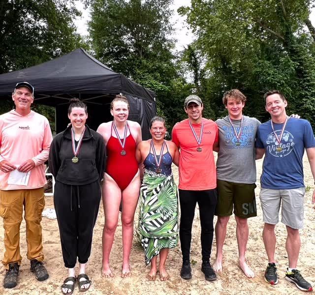 Group of seven people with medals pose on a sandy beach.