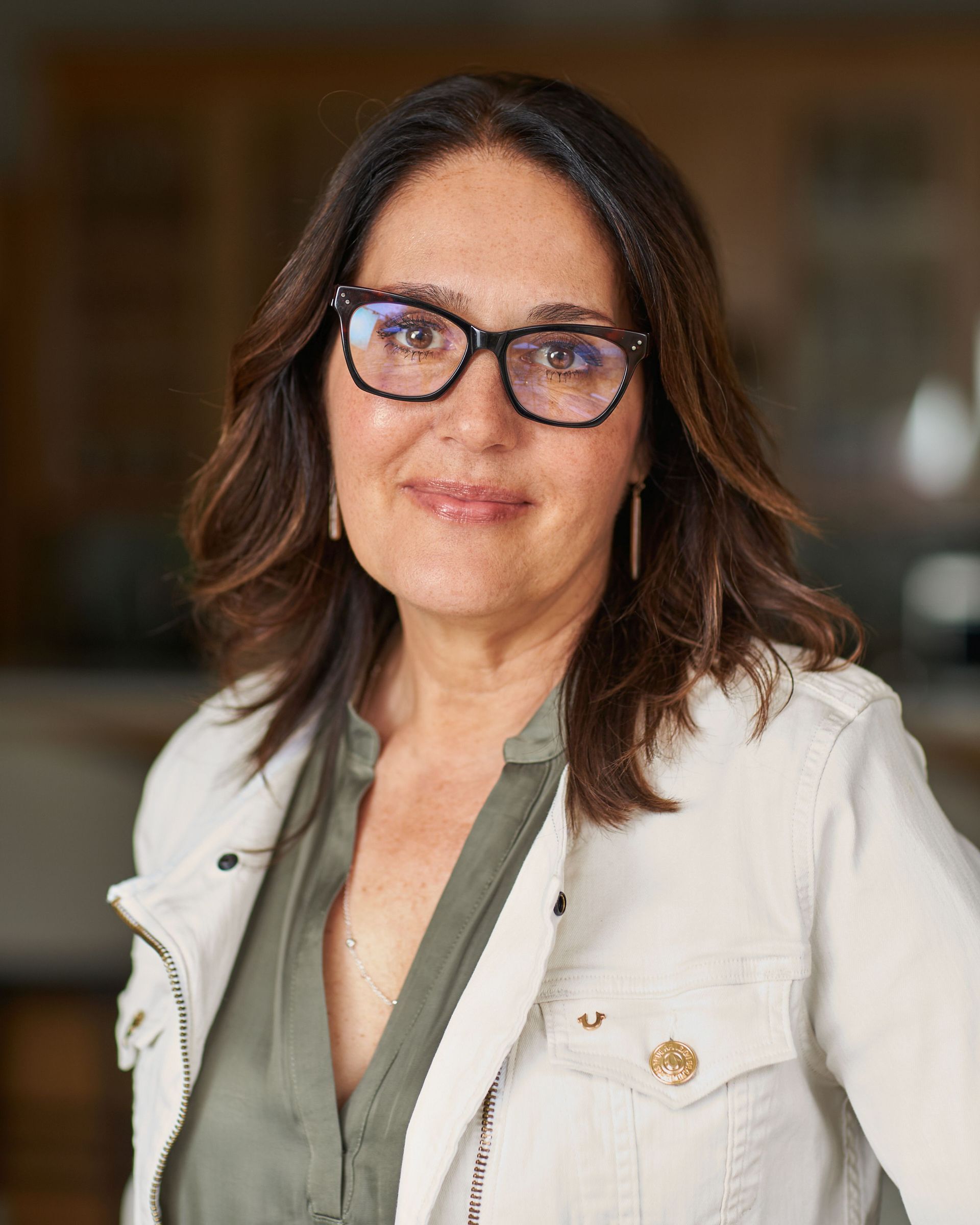 a woman wearing glasses and a white jacket smiles for the camera