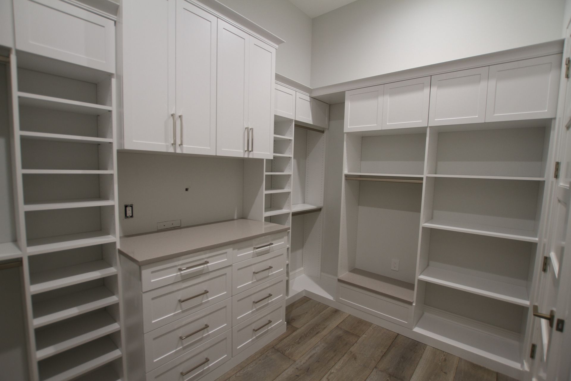 An empty walk in closet with white cabinets and shelves.