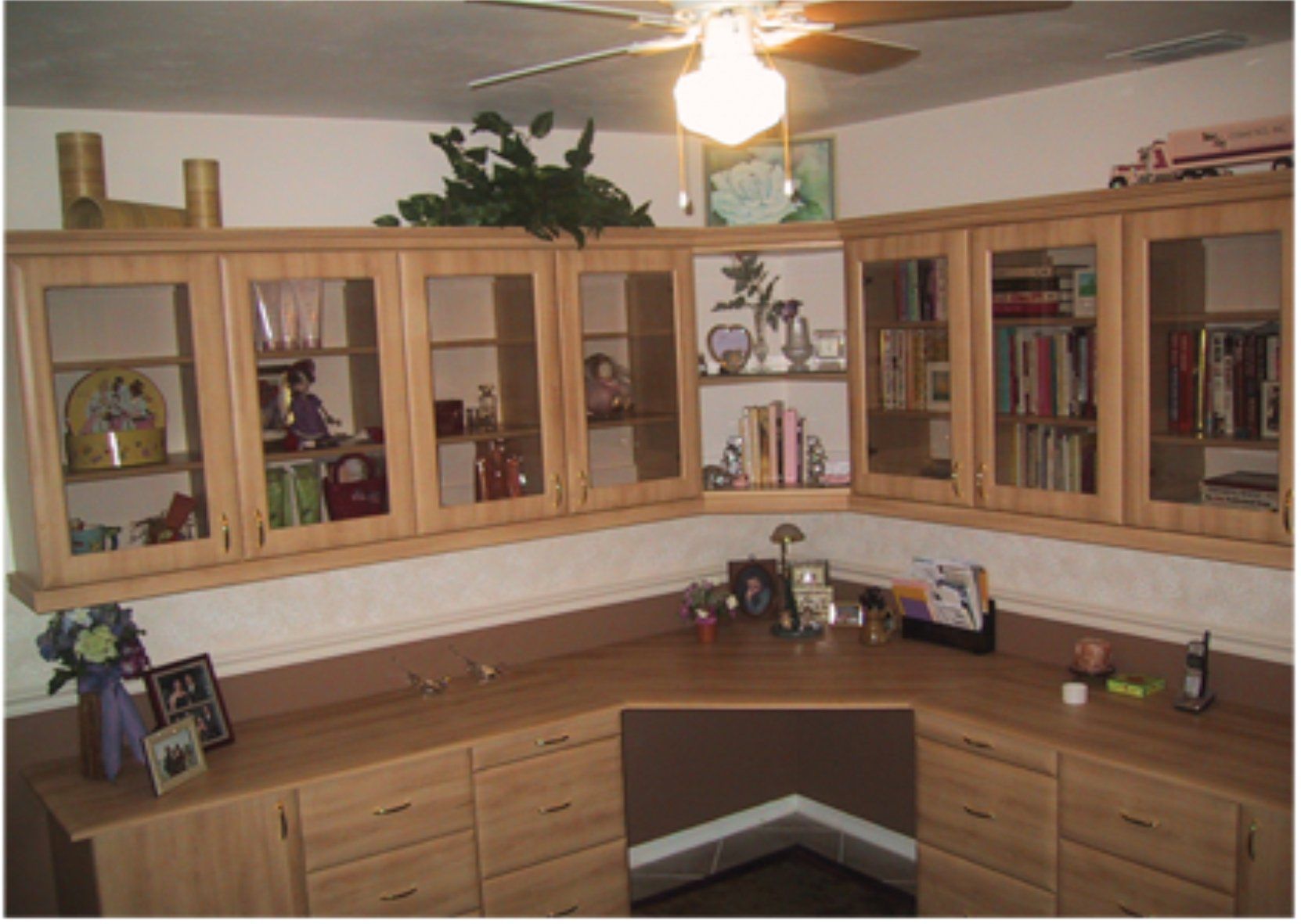 A corner of a room with a desk and a ceiling fan