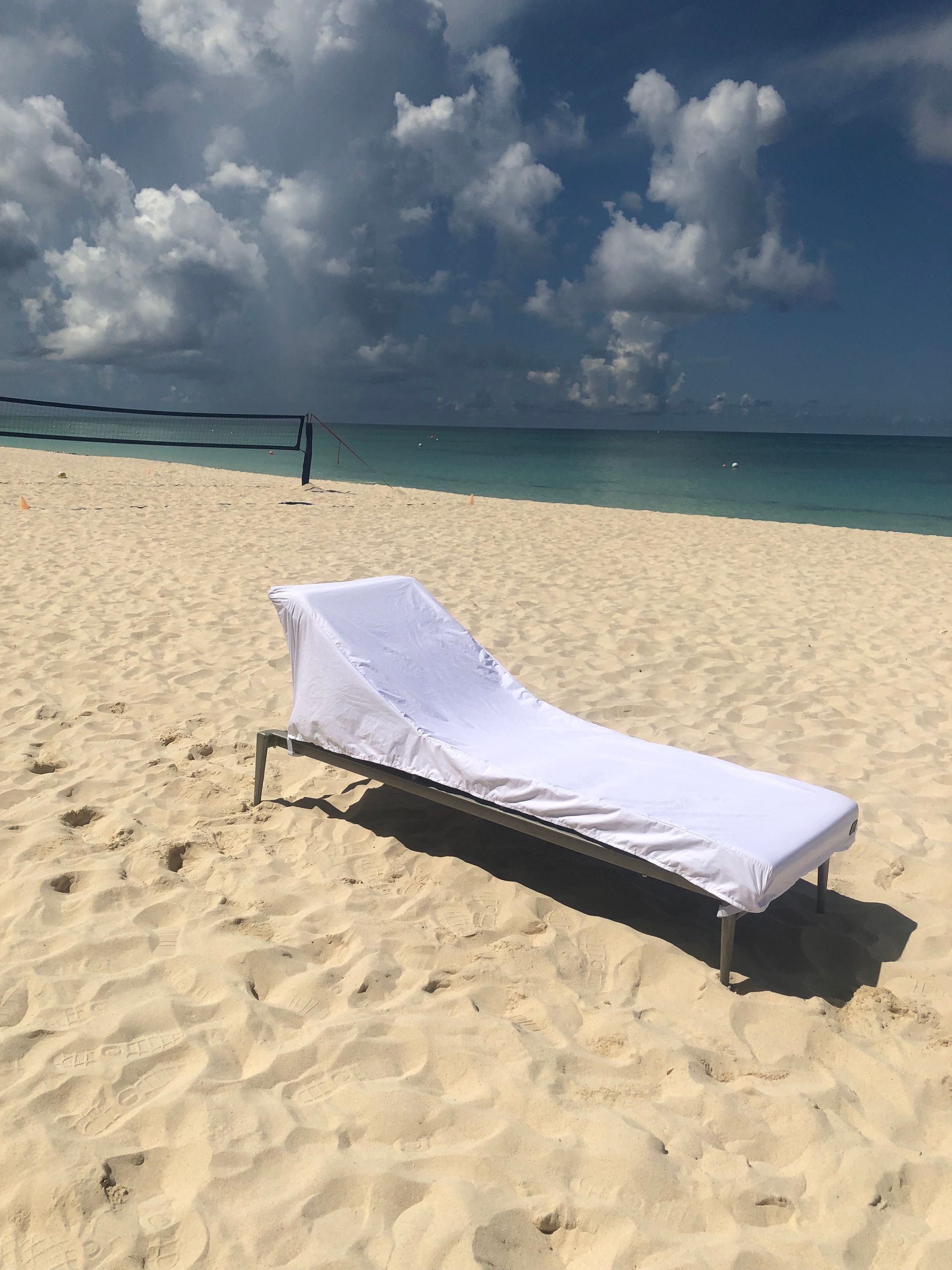 Beach scene: A white lounge chair with a white cover sits on a sandy beach.