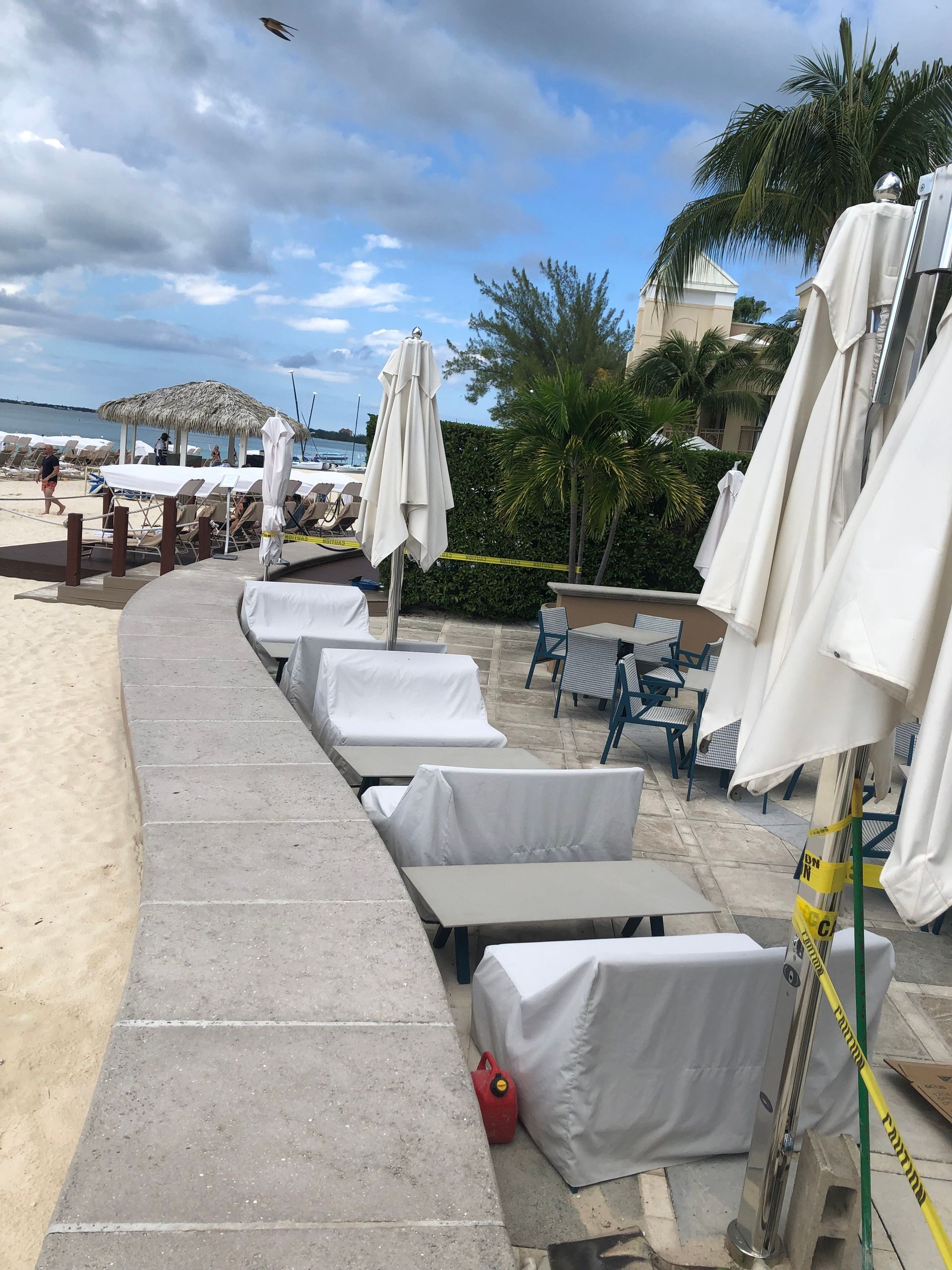 Beachside seating area with covered couches and tables under closed white umbrellas.