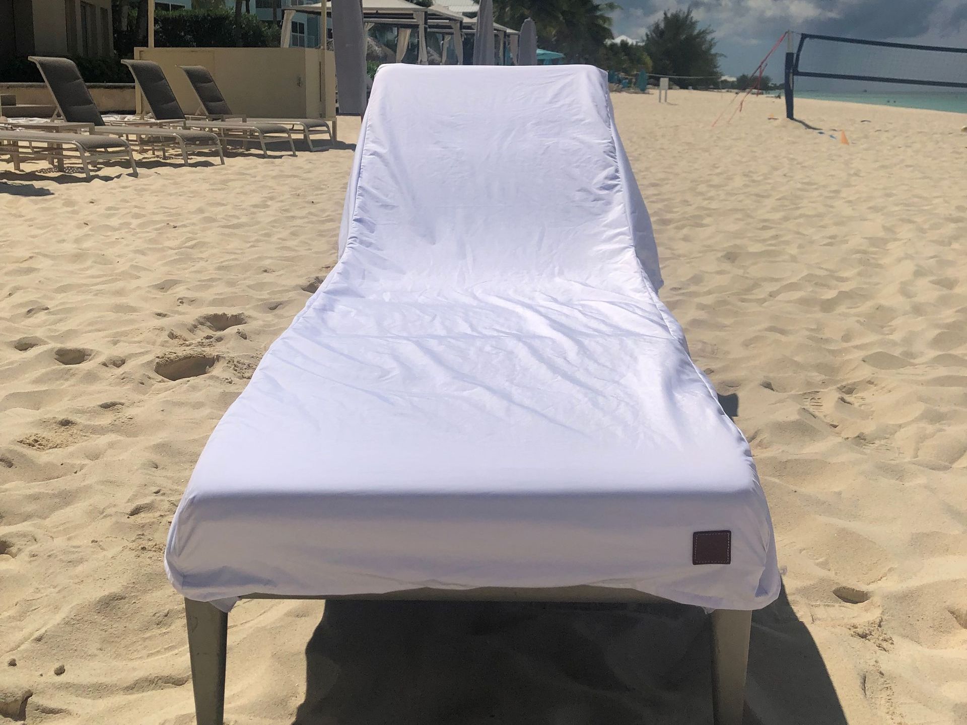 White beach chair covered with a white towel on a sandy beach, under the sunlight.
