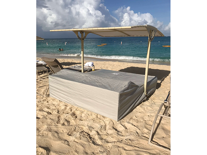 A beach cabana on a sandy shore, under a cloudy sky. The cabana is covered, with the ocean in the background.