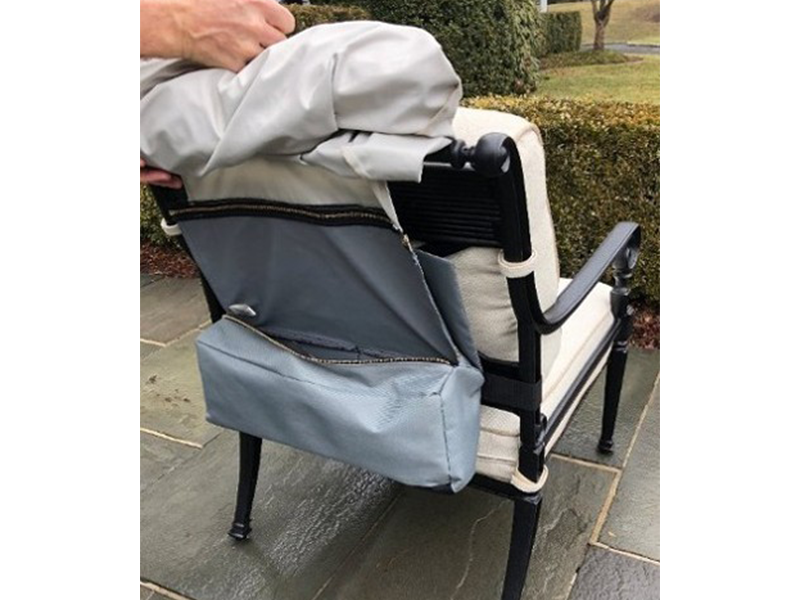 A person placing a light gray chair cover over a black and white outdoor chair. The cover has a pouch on the back.